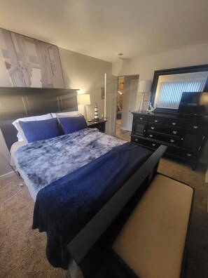 Hotellihuone, jossa on sänky, lipasto, televisio ja ovi, joka johtaa toiseen huoneeseen.