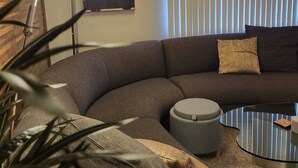 A modern living room with a curved sectional sofa, a round coffee table, and a floor lamp. - Galaxy on Medical Mile Come Thrive! (Grand Rapids)