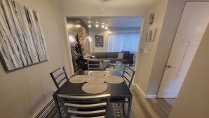 A dining area with a black table, four chairs, and a patterned rug. There is a plant and a sofa in the background. - Galaxy on Medical Mile Come Thrive! (Grand Rapids)