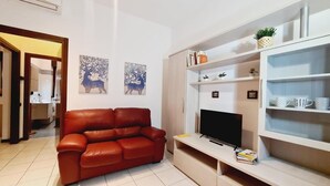 Una sala de estar con un sofá de cuero rojo, un televisor de pantalla plana y una estantería con objetos decorativos.