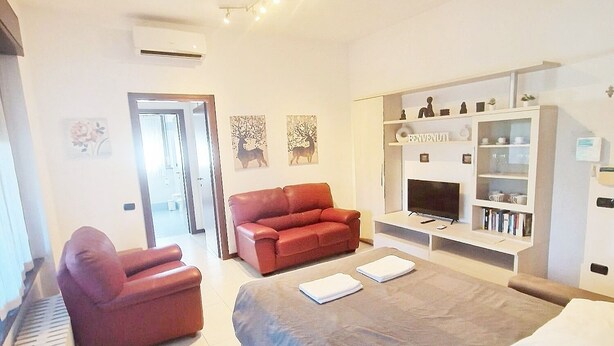 Una habitación de hotel moderna con una cama grande, un sofá rojo, un sillón rojo y un televisor sobre un mueble bajo.