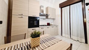 Una cocina moderna con armarios de madera clara, una estufa y una zona de comedor con camino de mesa a rayas y una planta en maceta.