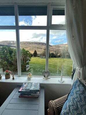 Een kamer met een groot raam met uitzicht op een groene omgeving met heuvels.
