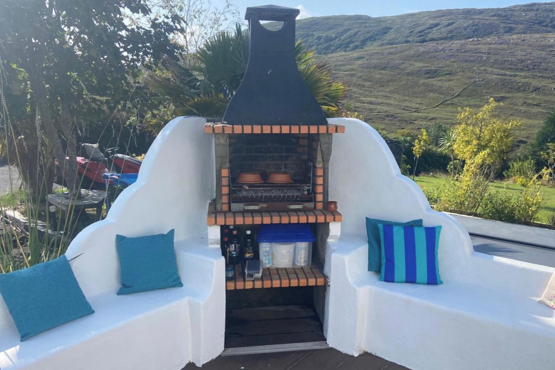 Una parrilla con chimenea, dos zonas de estar blancas con cojines azules y vistas a un paisaje montañoso.