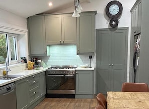 A kitchen with grey cabinets, a stove, and a clock on the wall. - Shantalla West Cork Farmhouse With Hot Tub & Sauna (Glanycarney)