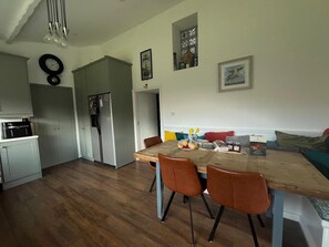 A modern kitchen with a refrigerator, a dining table with chairs, and a sofa in the living area.