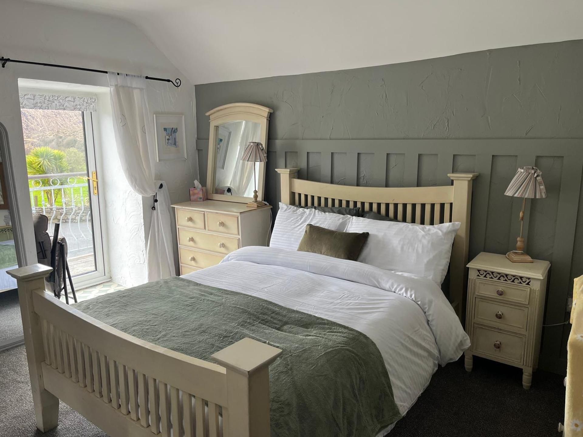 Ein Schlafzimmer mit einem Bett, einem Schminktisch, einem Nachttisch, einer Lampe und einem Fenster mit Vorhängen.