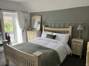 A bedroom with a bed, a dresser, a nightstand, a lamp, a mirror, and a window with curtains.