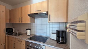 A kitchen with wooden cabinets, a microwave, a kettle, a toaster, and a coffee maker. - Modern vacation apartment "Wellenkieker" with balcony and parking space in Graal-Müritz (Graal-Müritz)