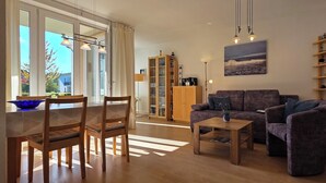 A living room with a sofa, coffee table, and chairs. There is a bookshelf and a painting on the wall. - Modern vacation apartment "Wellenkieker" with balcony and parking space in Graal-Müritz (Graal-Müritz)