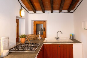 A kitchen with a gas stove, wooden cabinets, a sink, and a hanging light fixture.