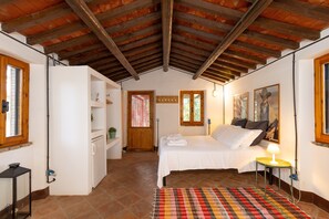 A bedroom with a bed, a bedside table with a lamp, a window, and a door leading to another room.