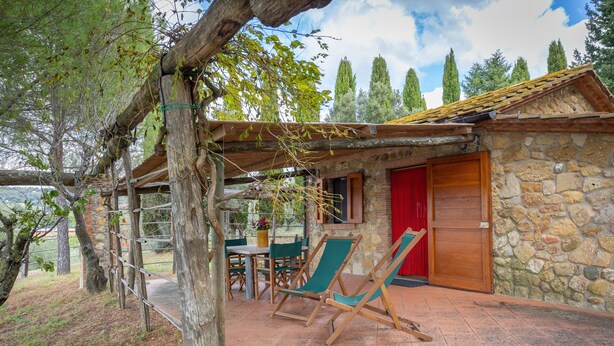 A stone building with a red door, a wooden pergola, and a table with chairs outside. - Holiday Home 'I Mandrioli' with Private Terrace, Wi-Fi and Air Conditioning (Casale Marittimo)