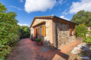 A stone house with a tiled patio, a small garden, and a clear blue sky.