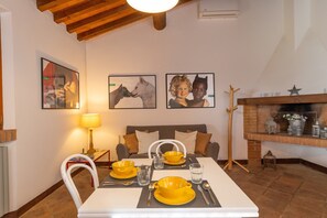 A dining area with a table set for two, a sofa, a fireplace, and artwork on the walls. - Holiday Home 'La Baciosa' with Private Terrace, Wi-Fi and Air Conditioning (Casale Marittimo)
