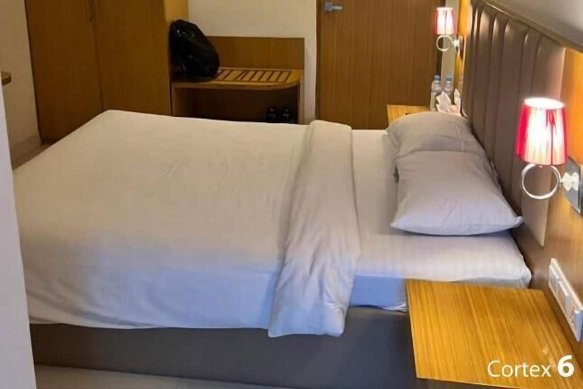 Habitación de hotel con cama, mesita de noche, lámpara y armario.