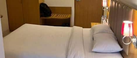 Habitación de hotel con cama, mesita de noche, lámpara y armario.