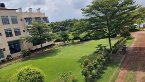 A well-maintained lawn with a paved path, a building with multiple windows and a water tank, and a motorcycle parked by the path. - Shalban Green Resort (Gazipur)