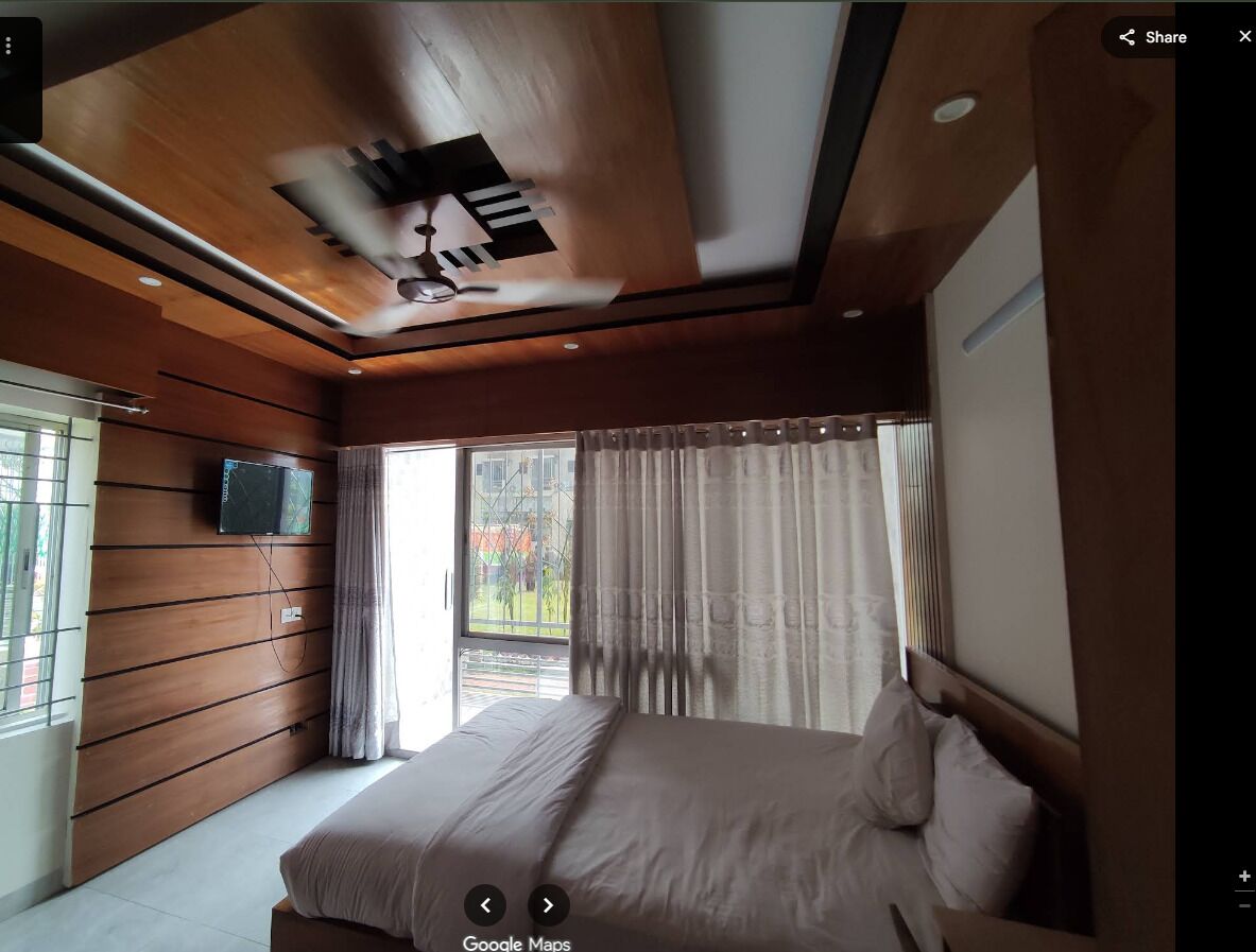 A bedroom with a bed, a television mounted on the wall, and a window with curtains.