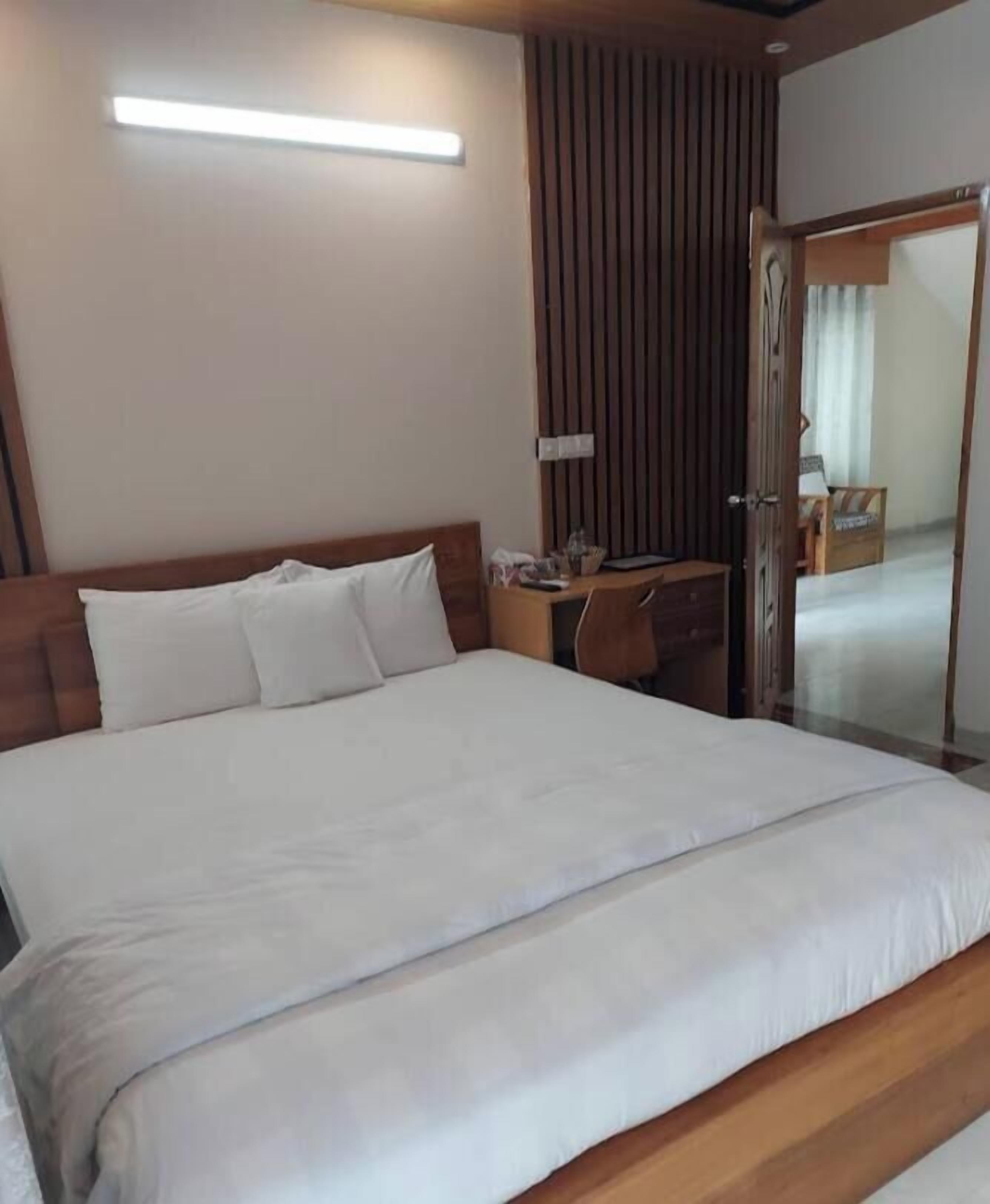 A neatly made bed with white linens, a wooden headboard, and a bedside table with a lamp.
