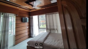 A bedroom with a bed, a ceiling fan, wooden panel walls, a window with curtains, and a door. - Shalban Green Resort (Gazipur)