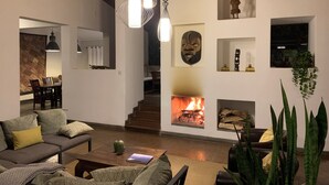 Un vaste espace de vie comprenant un salon avec cheminée, un coin repas et un escalier menant à l’étage supérieur.