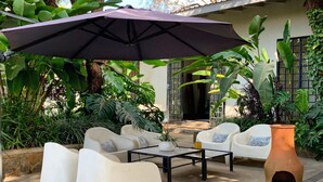 Un espace patio avec des chaises en plastique blanches, une table basse noire et un grand parasol foncé.