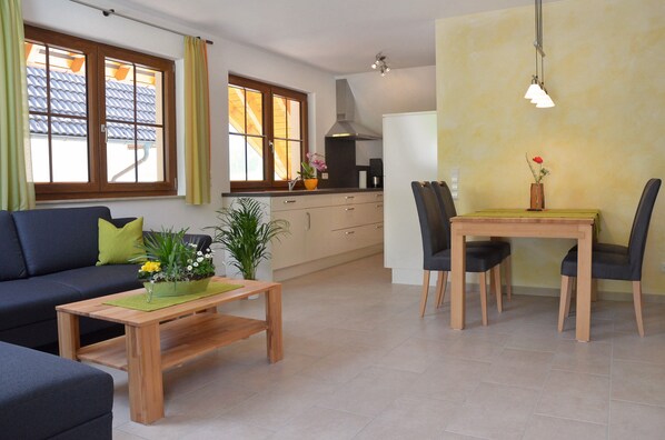 Un salon avec un canapé, une table à manger avec des chaises, un coin cuisine avec des placards et une fenêtre avec des rideaux.