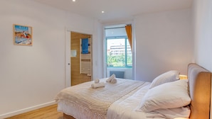 A bedroom with a bed, a window with curtains, a door, and a wall with a picture.