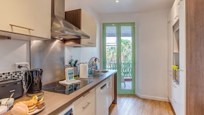 A compact kitchen with modern appliances, a built-in oven, and a view of the balcony through a green door.