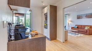 A modern kitchen with a built-in espresso machine, a dining area with a wooden table, and a living room with a sofa and a painting on the wall.