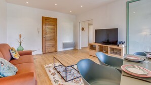 A modern living room with a sofa, chairs, a TV, and a dining area with plates and glasses.