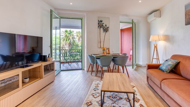 A modern living room with a flat-screen TV, a wooden entertainment unit, a sofa, and a dining area with a table and chairs.