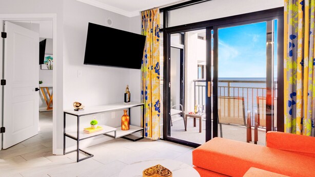 Ett modernt vardagsrum med en platt-TV, ett litet runt bord och en knallorange soffa.