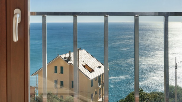 Un balcón con vista al mar, un edificio de fachada clara y una barandilla de metal.