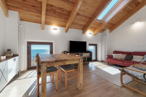 A spacious living area with a wooden ceiling, a large TV, a red sofa, and a dining table with chairs.