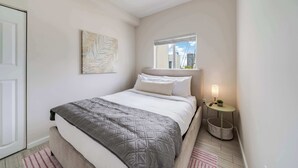 Une chambre à coucher avec un lit, une fenêtre donnant sur la ville, une table de chevet avec une lampe et une œuvre d’art accrochée au mur.