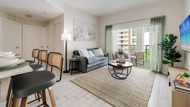 Un salon comprenant un canapé, des fauteuils, une table basse, une table à manger avec des chaises, et donnant sur l’extérieur.