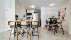 A modern kitchen with a dining area, featuring a kitchen island, bar stools, and a small table with chairs. - Edgewater Pad- Balcony, Parking and Prime Location (Miami)