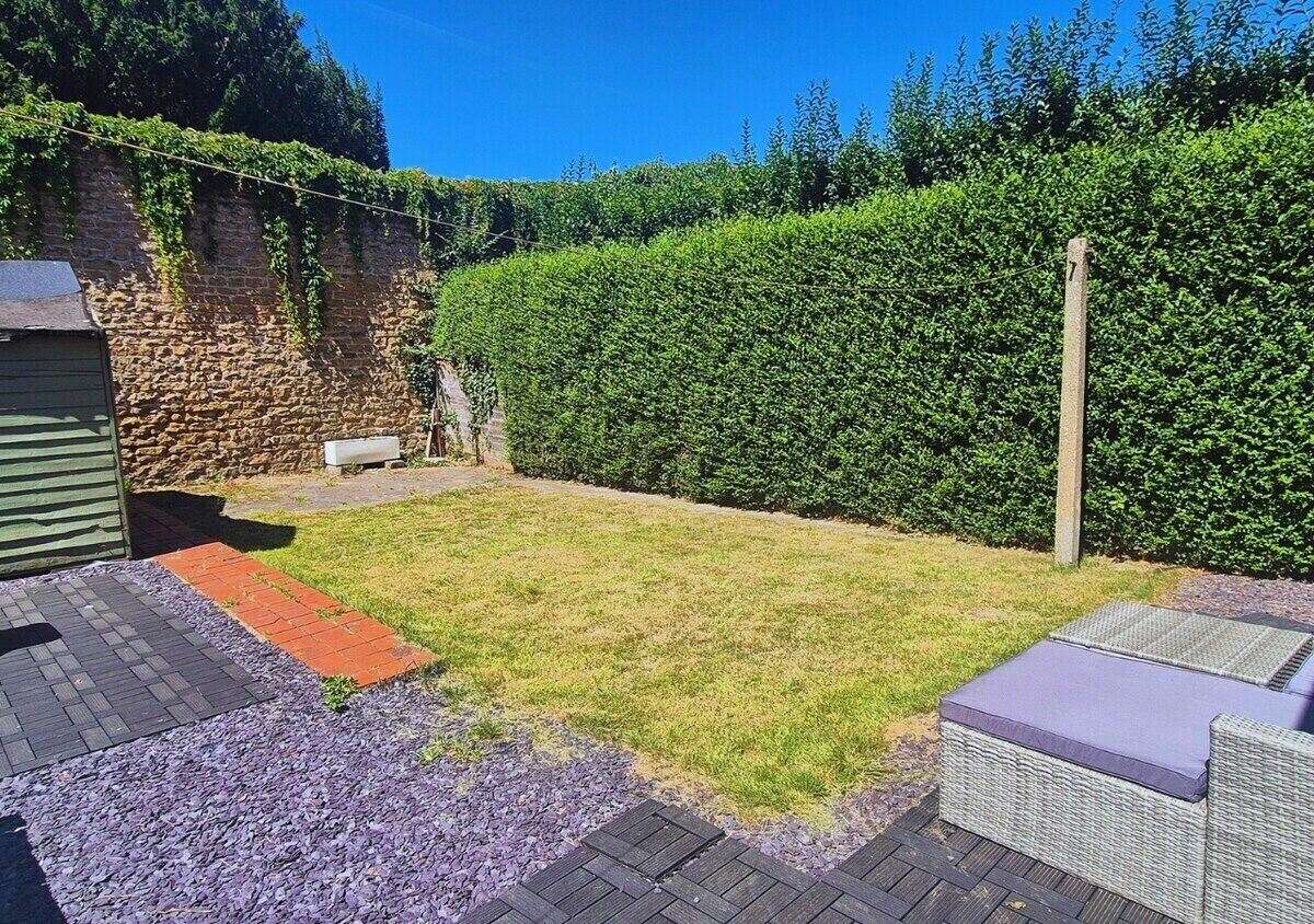 A backyard with a grassy lawn, a stone wall, a wooden fence, and a hedge.