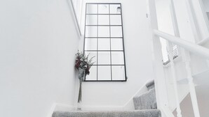 A staircase with a white railing, a clear glass window, and a vase with flowers. - Cosy 2BR House on Quiet Street (Nottingham)