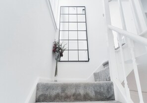 En trappa med ett vitt räcke, ett stort fönster av klart glas och en vas med blommor.