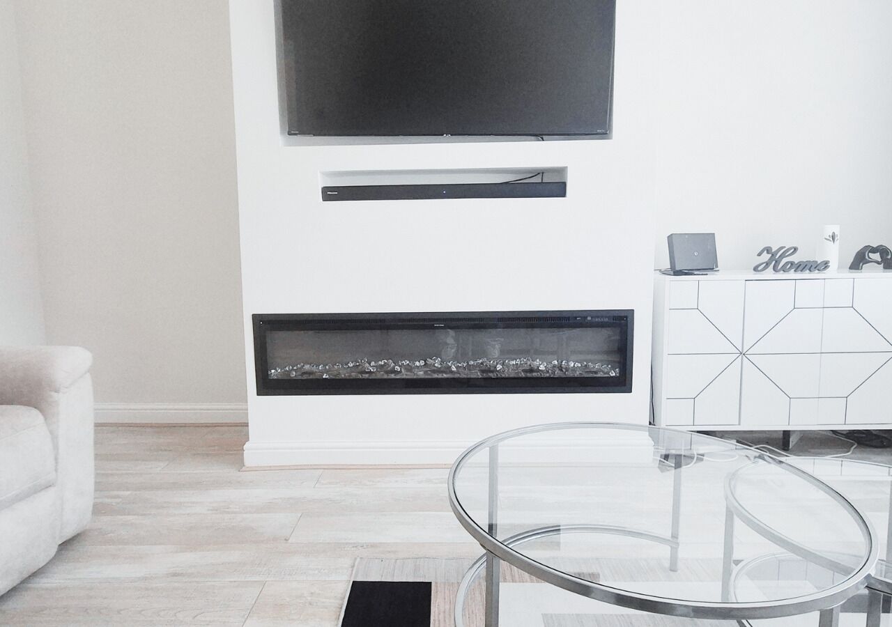 Una sala moderna con una mesa de centro de vidrio, un televisor de pantalla plana sobre la chimenea y un armario blanco con diseño de mosaicos geométricos.