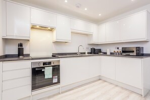 A modern kitchen with white cabinets, a built-in oven, a microwave, and a sink. - Toast Stays - The Slate at Parsons House (Washington)