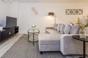 A modern living room with a grey sofa, a flat-screen TV, a small side table with a vase, and a floor lamp. - Toast Stays - The Slate at Parsons House (Washington)