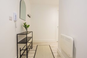A hallway with a black metal shelf, a mirror, a wall-mounted phone, a small plant, and a radiator. - Toast Stays - The Slate at Parsons House (Washington)