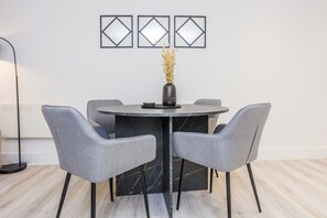 Ein moderner Essbereich mit einem Marmortisch, grauen Polsterstühlen und einer Vase mit Trockenblumen.