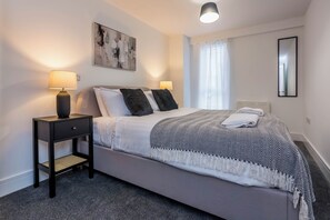 A modern bedroom with a bed, two bedside lamps, a small nightstand, a wall-mounted mirror, and a window with curtains. - Toast Stays - The Slate at Parsons House (Washington)