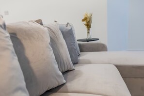 A modern sofa with multiple cushions in a neutral color palette, positioned against a plain wall with a small side table and a vase of flowers. - Toast Stays - The Slate at Parsons House (Washington)