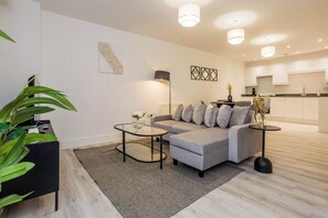 A modern living room with a grey sofa, a glass coffee table, and a black side table. There is a plant on the left and a floor lamp in the center. - Toast Stays - The Slate at Parsons House (Washington)